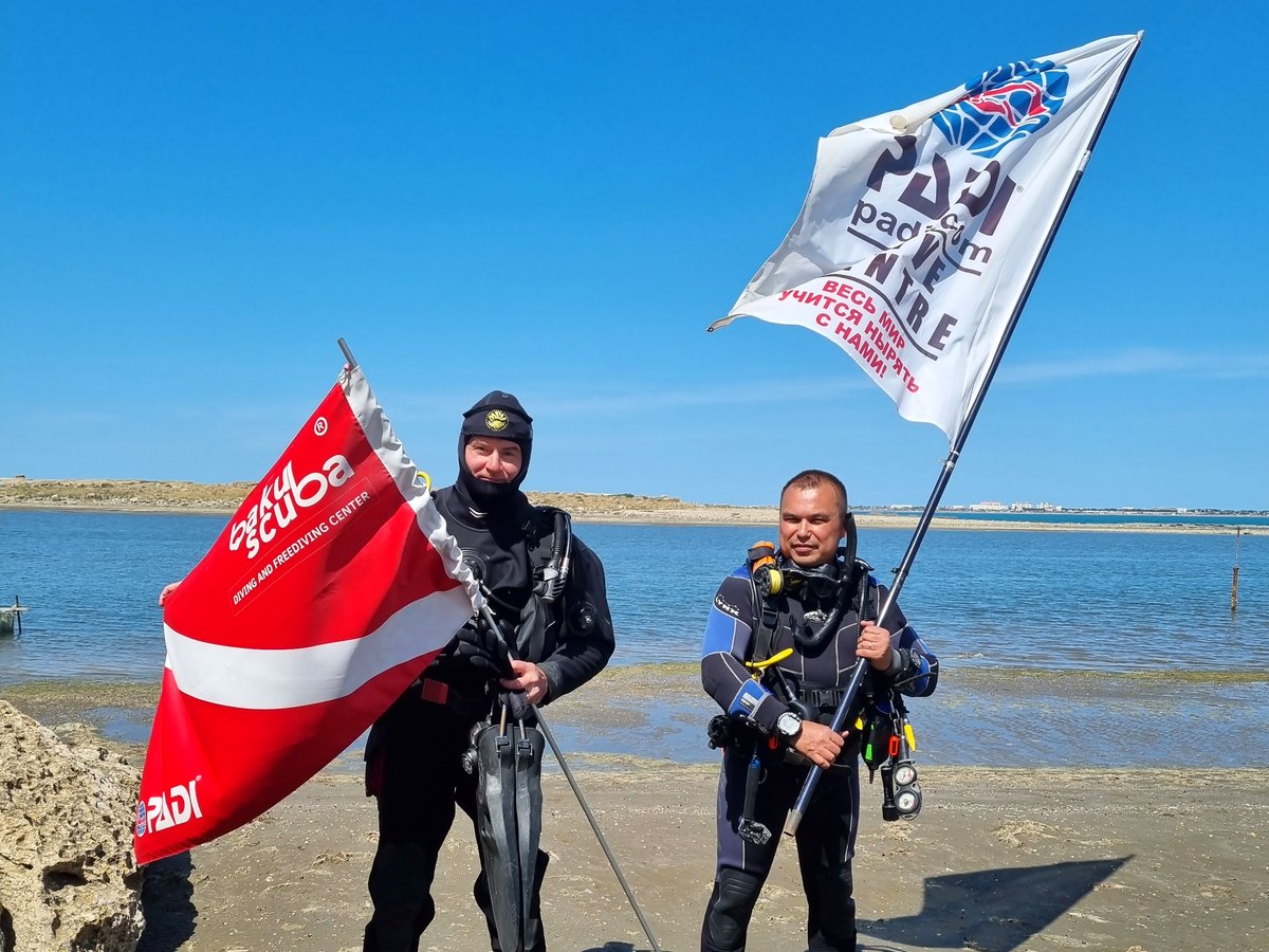 Инструкторы Baku Scuba с флагами PADI и Baku Scuba на берегу Каспия